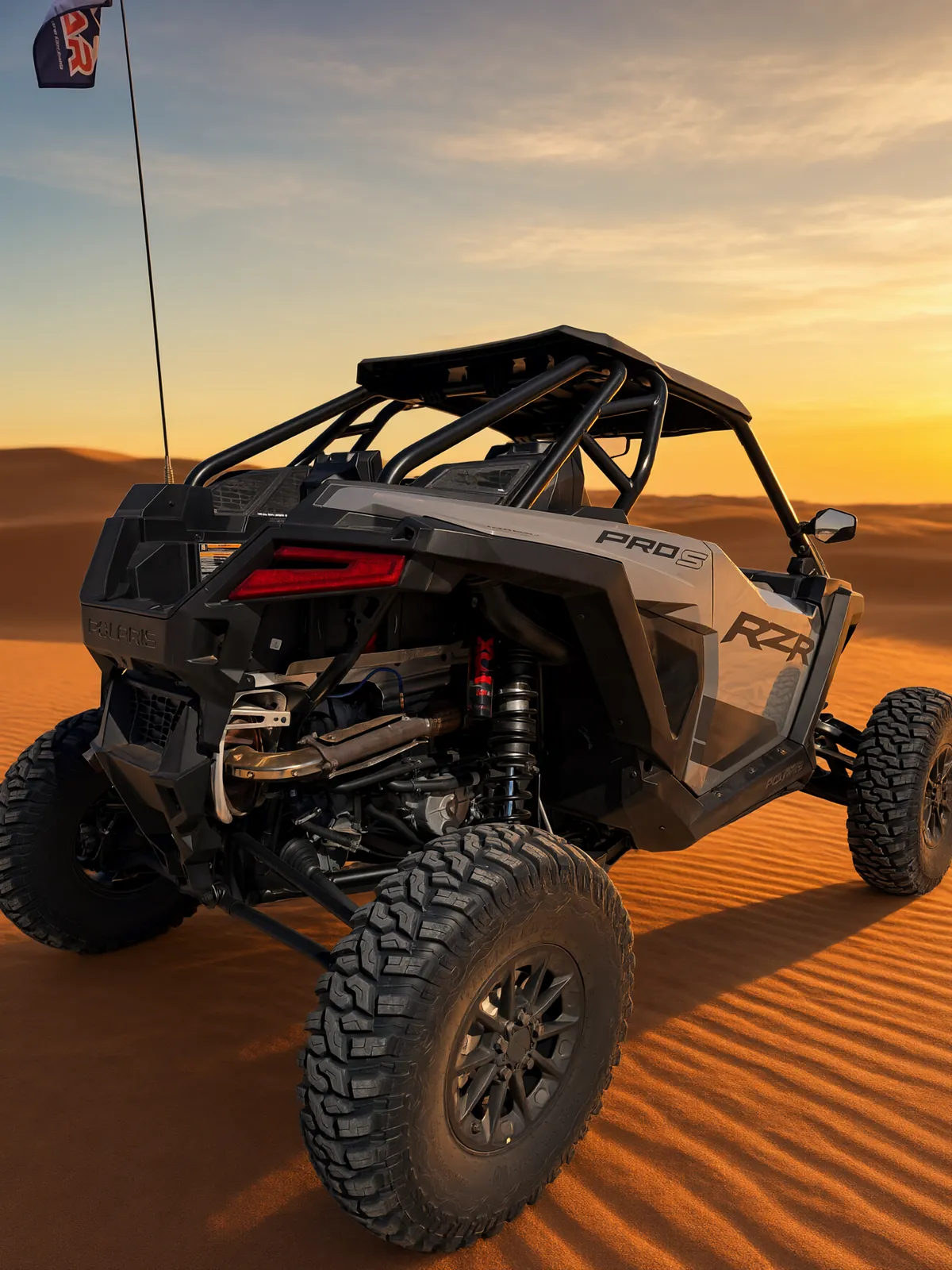 Polaris RZR Pro S Ultimate "Ninja" on wind-rippled orange sand dunes at golden hour, rear view showing the Pro S badge, exhaust and rear suspension
